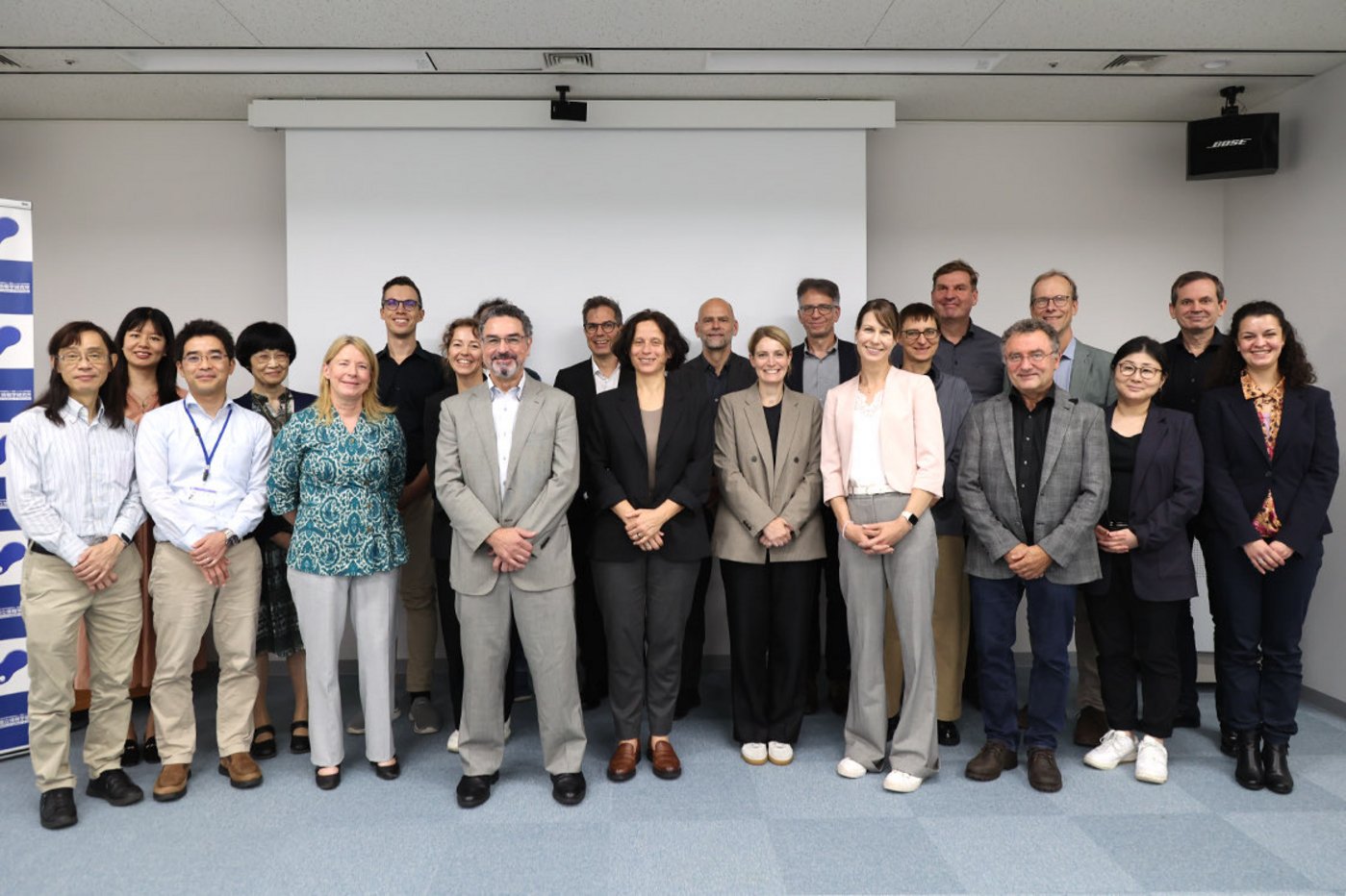 Gruppenbild der Teilnehmenden der Delegationsreise nach Japan, alle stehen nebeneinander und gestaffelt der Kamera zugewandt vor einer hellen Wand.